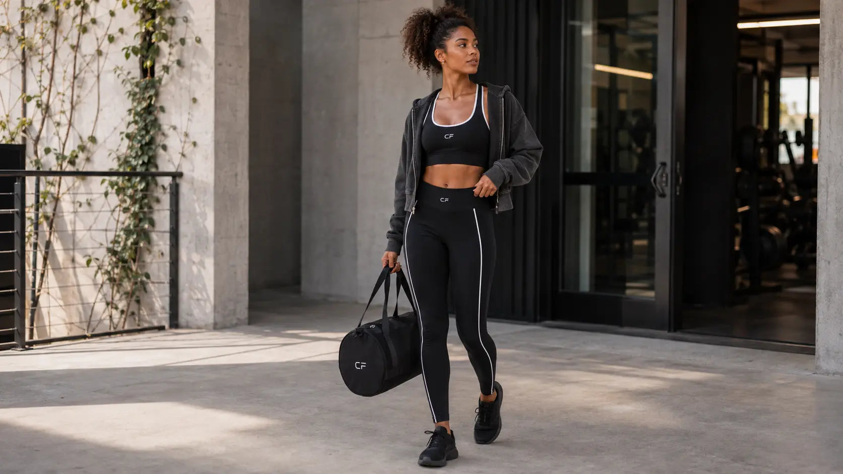 Woman arriving at a modern gym in a CRAMPFIT black activewear outfit with gym bag