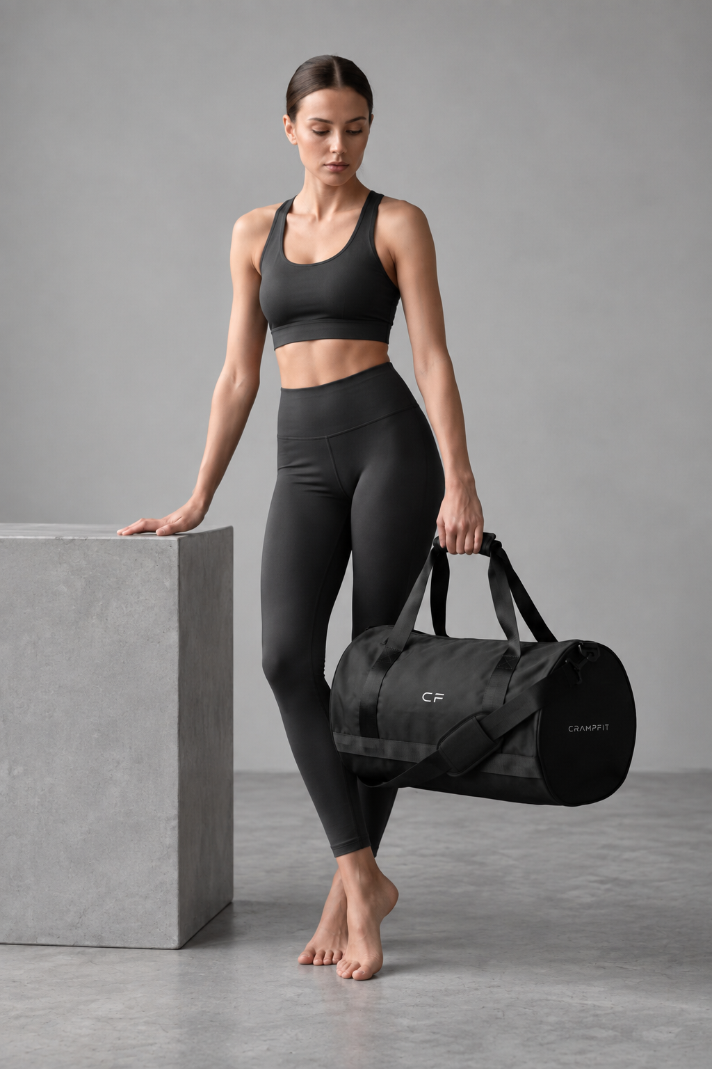 Woman carrying CRAMPFIT black gym duffel bag in full-body studio photo