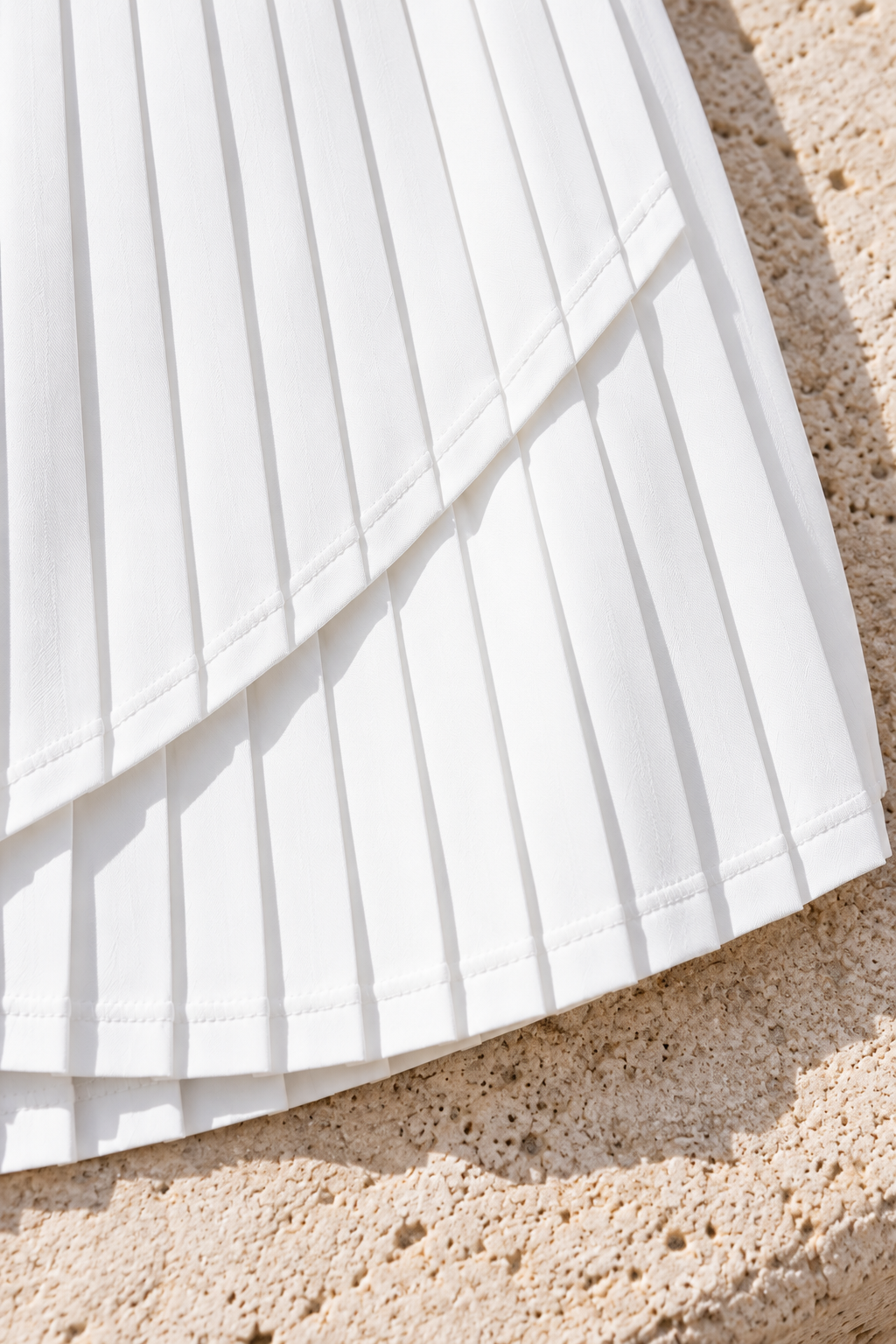 CRAMPFIT Pleated Performance Skort in white, close-up of pleats and overlapping curved hem