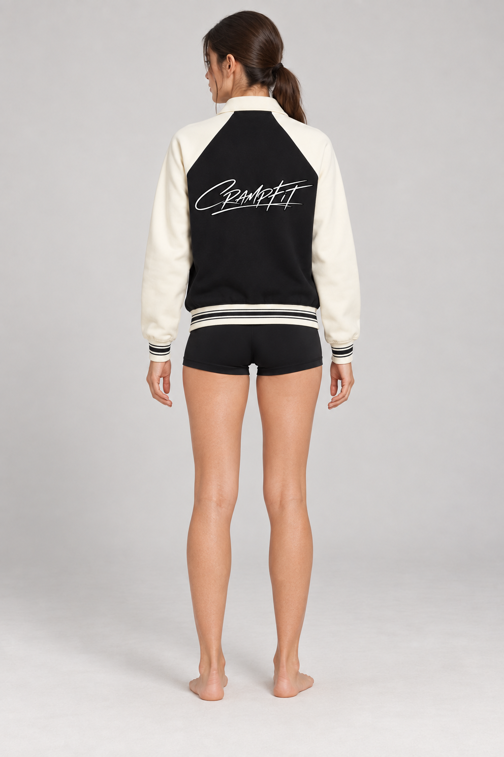 CRAMPFIT Raglan Varsity Jacket in black and cream, back logo view on a slim female model