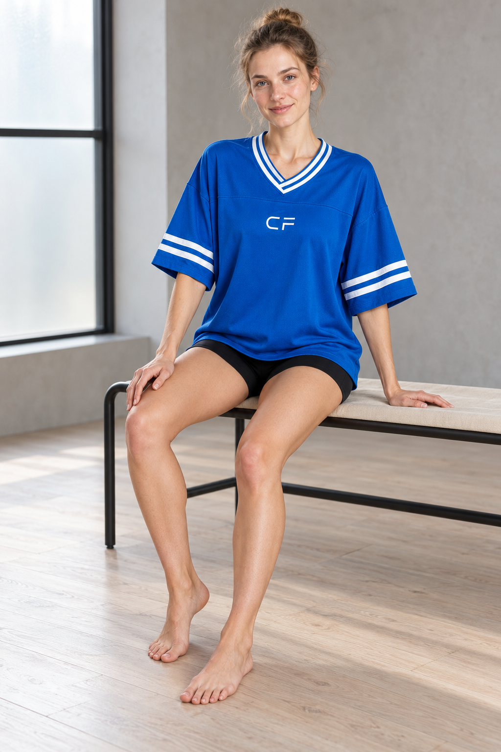 Model seated in CRAMPFIT blue boxy jersey with white sleeve stripes in natural studio light.