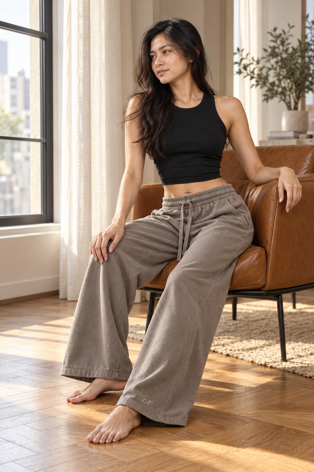 Model seated in CRAMPFIT espresso wide-leg cotton sweatpants in natural window light.