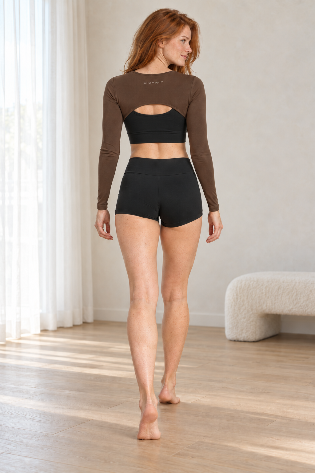 CRAMPFIT brown cutout shrug, rear view showing the curved back hem and CRAMPFIT branding. Styled over a separate black sports bra.