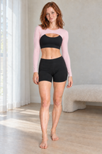 CRAMPFIT women's light pink cutout shrug, full-body front view showing long sleeves and curved front opening. Styled over a separate black sports bra.
