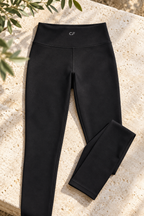 Black CRAMPFIT high-waist yoga leggings laid on stone, showing the wide waistband, CF logo, stitching and folded ankle hem.
