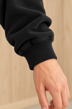 Close-up of CRAMPFIT black mockneck sweatshirt showing ribbed sleeve cuff, stitching and fabric texture.
