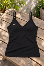 Black CRAMPFIT V-neck yoga tank laid on a wooden bench, showing its adjustable straps, shaped front seams, CF logo and fabric texture.