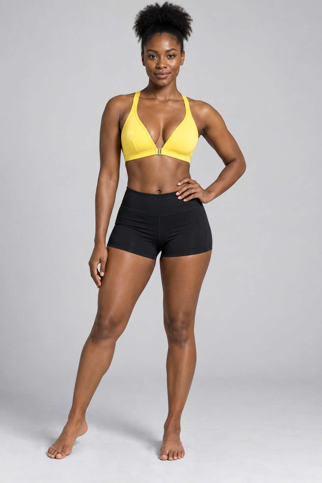 CRAMPFIT Women's Yoga Sports Bra - yellow front view, barefoot, styled with black workout shorts